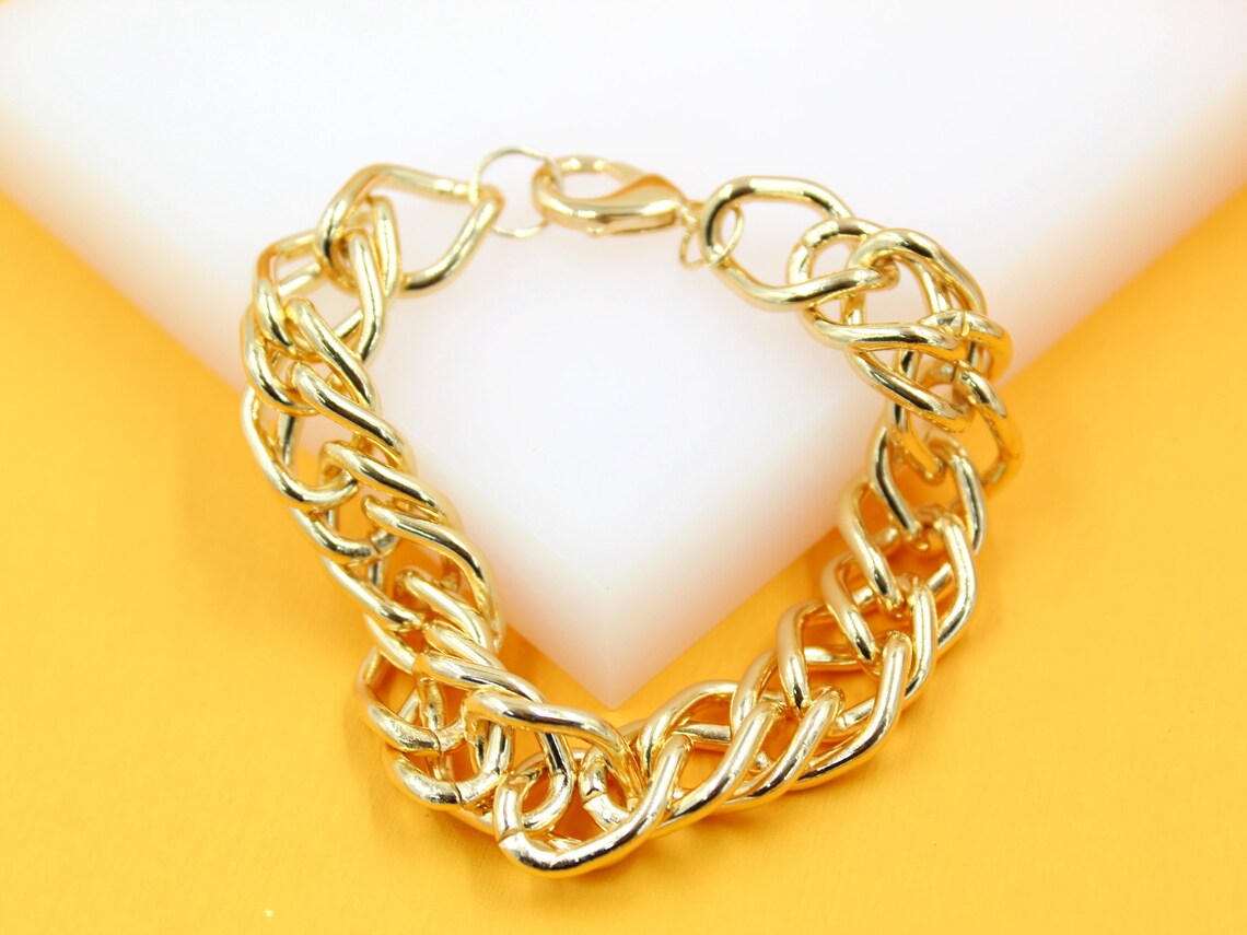 A chunky gold-plated chain bracelet rests on a white and yellow display surface.