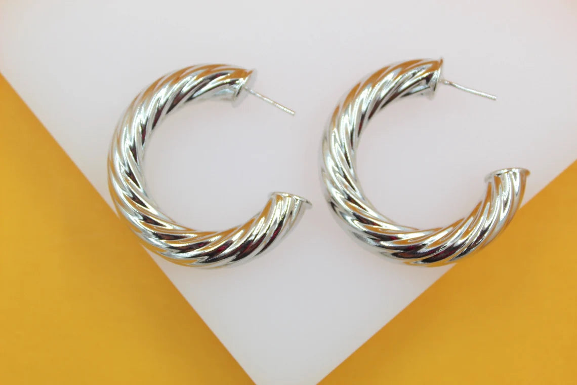 A pair of thick, silver-plated twisted hoop earrings rest neatly on a white and yellow display stand.
