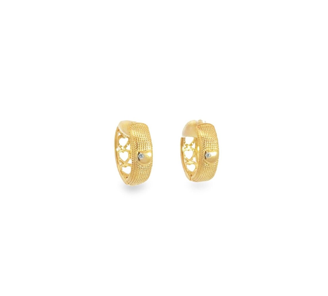 A pair of textured gold hoop earrings featuring cut-out heart patterns rests against a clean white background.