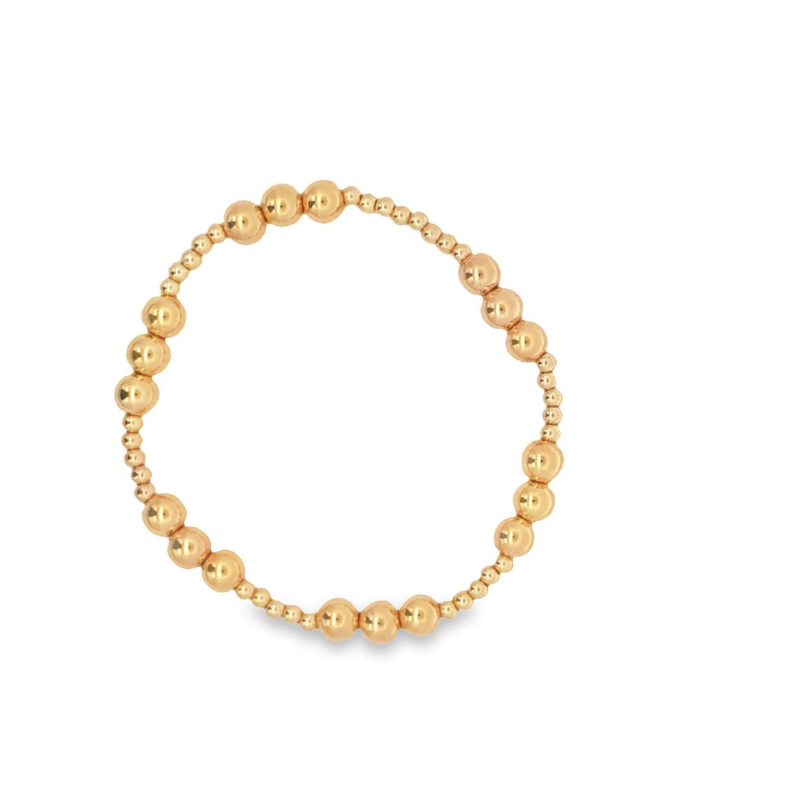 A delicate gold beaded stretch bracelet features a circular arrangement of polished metallic balls in varying sizes against a clean white background.