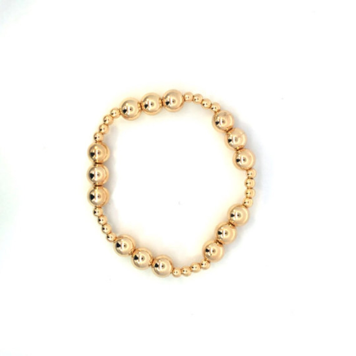 A gold beaded stretch bracelet rests against a plain white background, showcasing shiny metallic beads of graduating sizes.