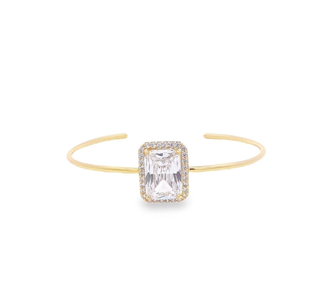 A delicate gold cuff bracelet showcases a large, emerald-cut cubic zirconia center stone surrounded by a sparkling halo of pave diamonds.