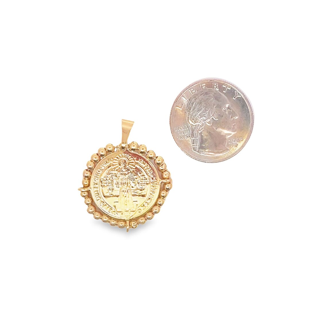 A round gold Saint Benedict pendant rests next to a US quarter coin to show scale.