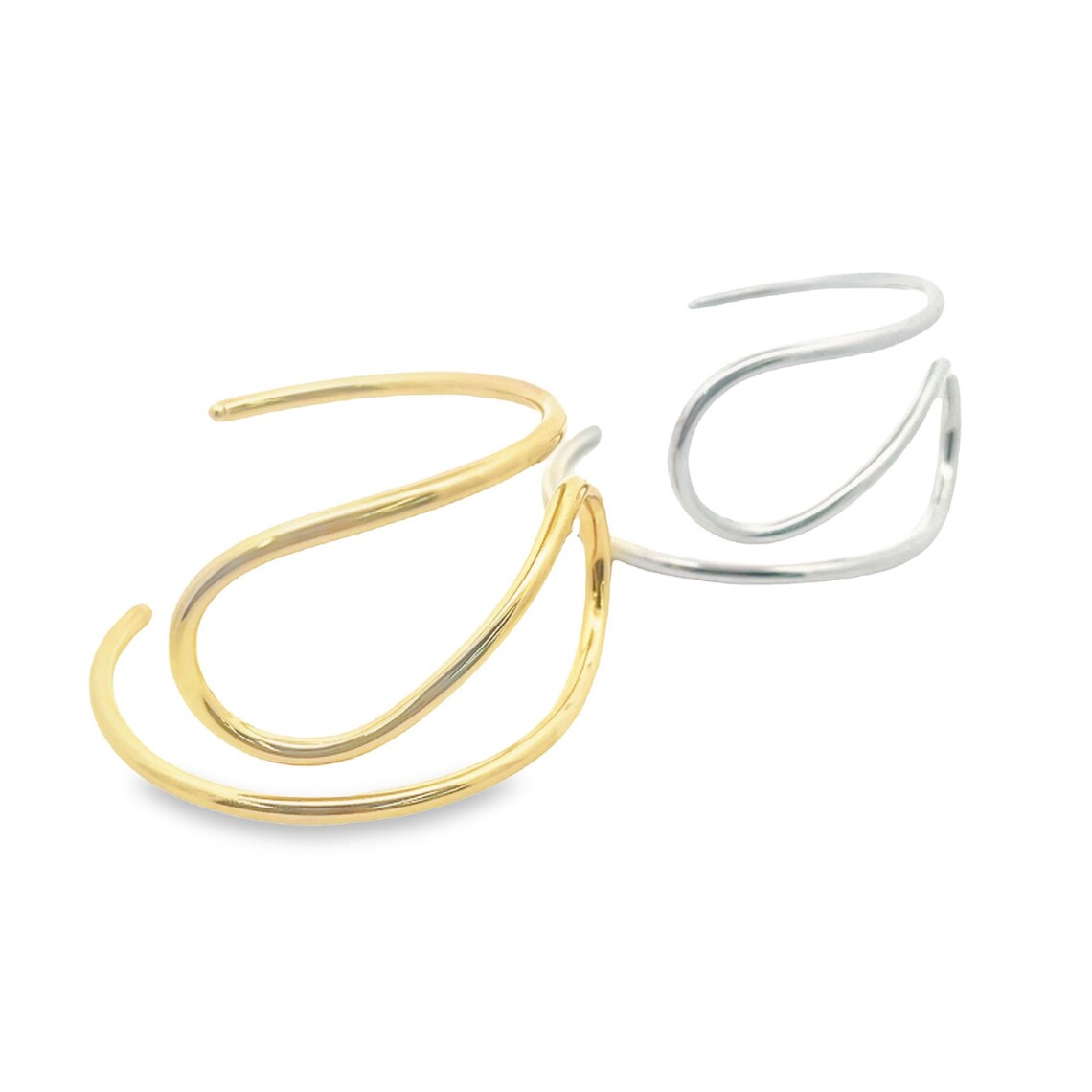 Two minimalist gold and silver ear cuffs feature sleek, abstract curved designs against a clean white background.