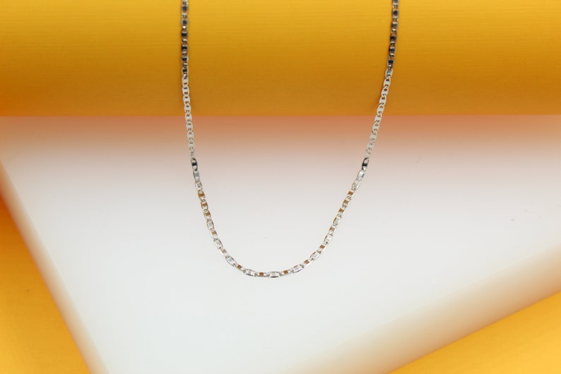 A delicate silver chain necklace drapes against a vibrant yellow and white backdrop.