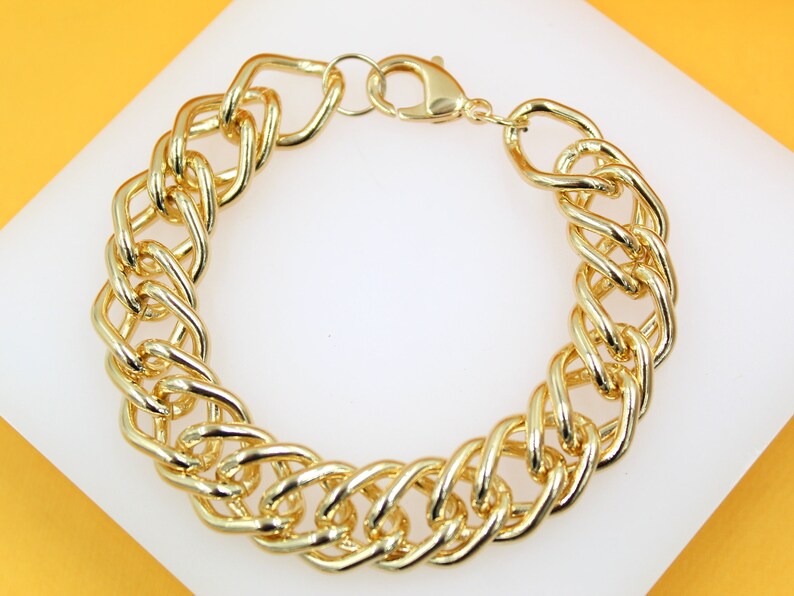 A thick, polished gold chain link bracelet rests against a white display surface.
