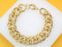 A thick, polished gold chain link bracelet rests against a white display surface.