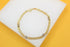A delicate gold-plated double chain bracelet with silver-accented stations rests on a white display surface against a vibrant yellow background.