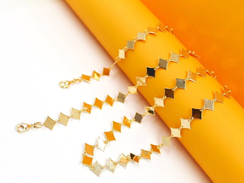 A gleaming gold rhombus-shaped link chain necklace rests elegantly against a vibrant orange and white background.