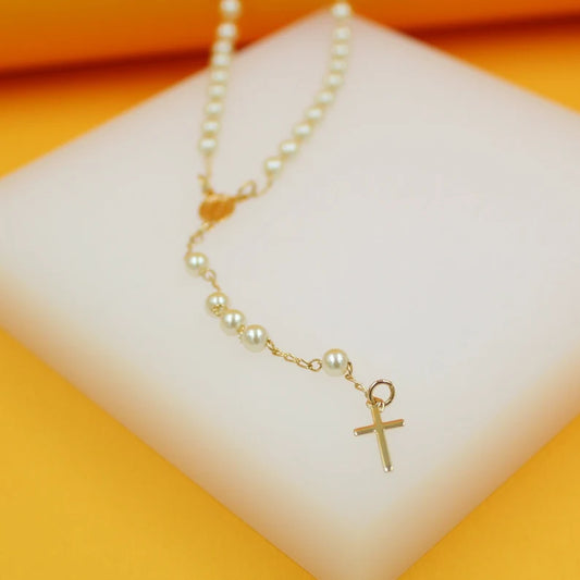 A delicate gold pearl rosary necklace rests on a white display block against an orange background.