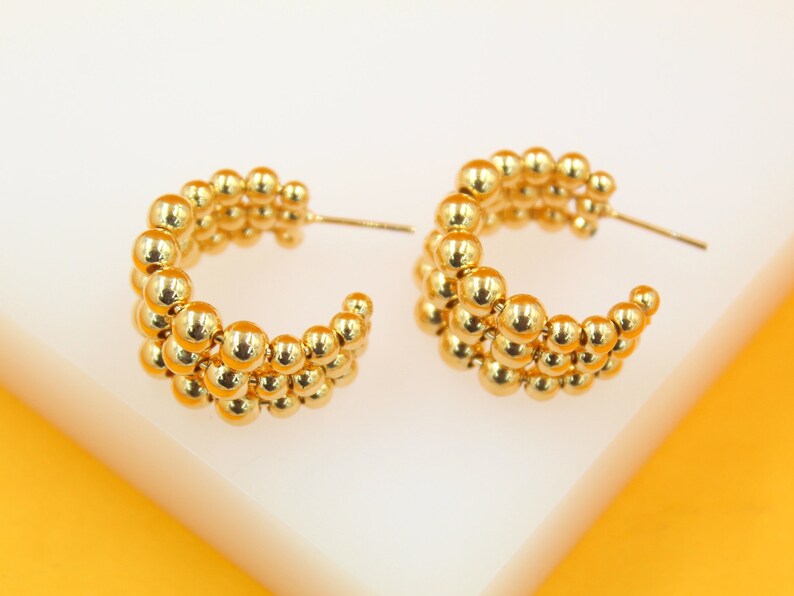 A pair of shiny gold multi-row ball hoop earrings rests on a clean white surface.