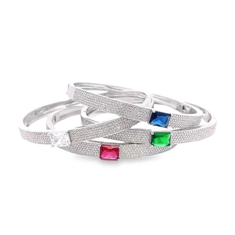 A stack of shimmering pave-set silver bangles features vibrant emerald-cut gemstones in red, blue, green, and clear.