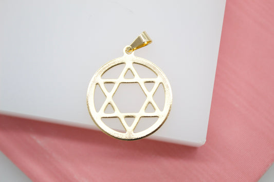 A polished gold Star of David pendant rests against a clean white surface with a soft pink background.