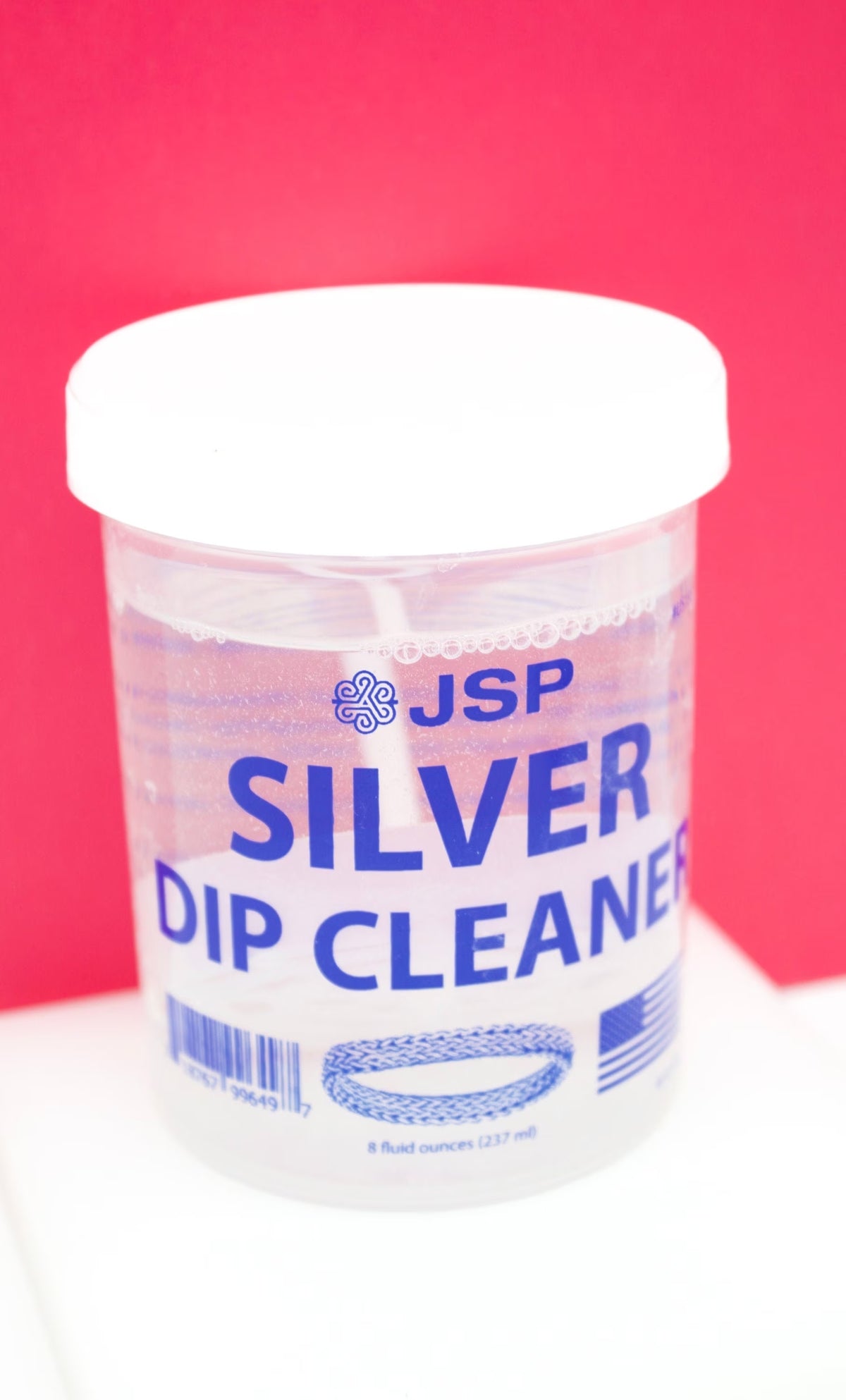 A jar of JSP silver dip cleaner sits against a bright pink background.