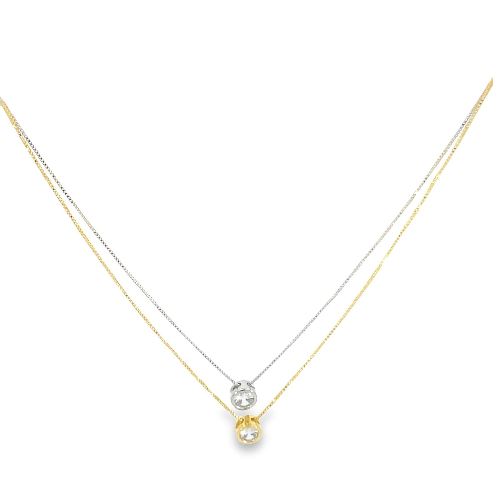 A layered two-tone necklace features a delicate yellow gold chain with a bezel-set diamond pendant resting above a matching white gold chain and diamond pendant.