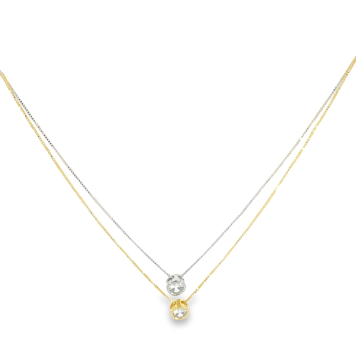 A layered two-tone necklace features a delicate yellow gold chain with a bezel-set diamond pendant resting above a matching white gold chain and diamond pendant.