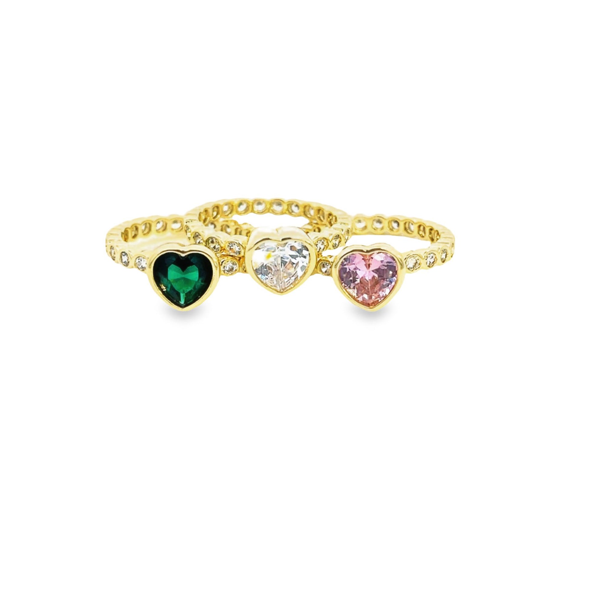 Three gold heart-shaped gemstone rings featuring a deep green emerald, a clear diamond, and a soft pink sapphire sparkle against a plain white background.