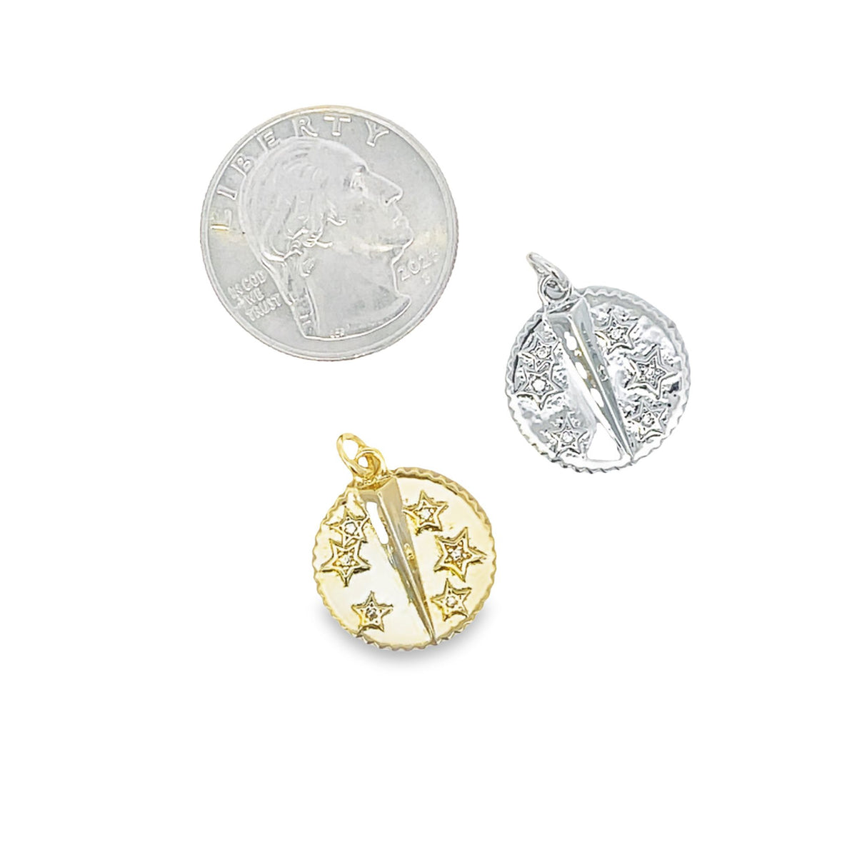 A dime rests next to two gold and silver star pendant charms on a white background.
