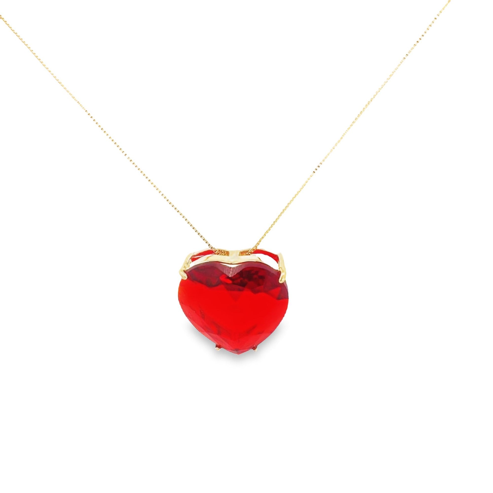 A delicate gold chain holds a vibrant red heart-shaped gemstone pendant against a clean white background.