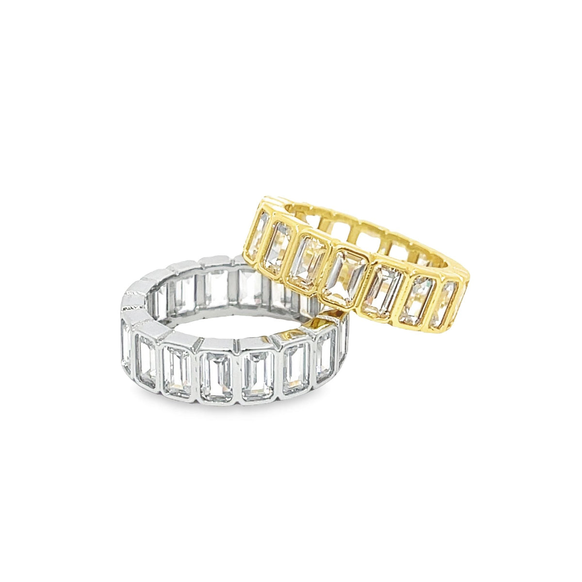 Two interlocking eternity bands featuring sparkling emerald-cut baguette stones in gold and silver rest against a clean white background.