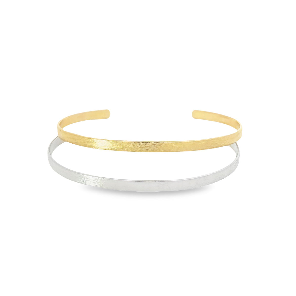 Two minimalist metal cuff bracelets, one gold and one silver, rest stacked on a white surface.