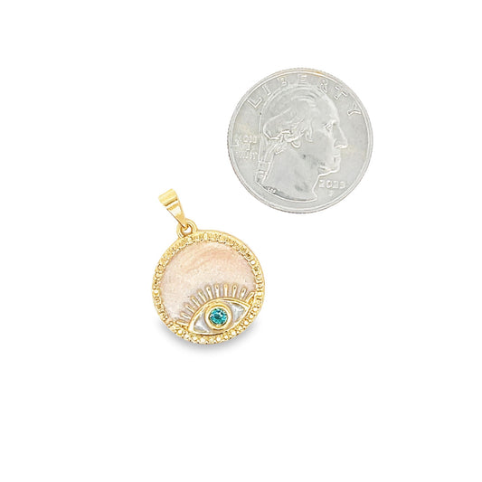 A round gold evil eye pendant with pink enamel and a blue crystal rests next to a US quarter coin for scale.