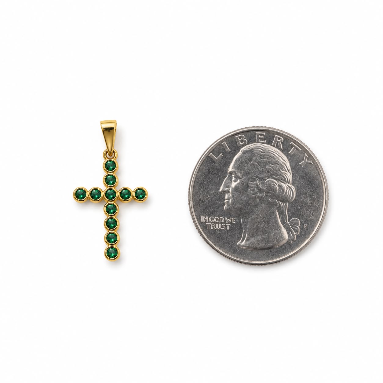 A gold cross pendant encrusted with green gemstones rests next to a US quarter coin for scale.