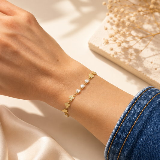A delicate gold chain bracelet featuring alternating butterfly charms and small white pearls adorns a woman's wrist.