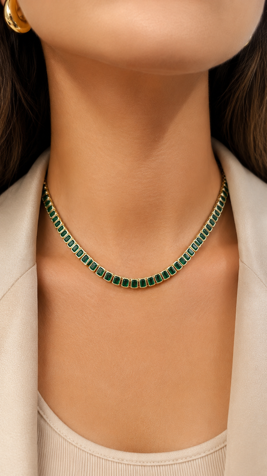 A woman wearing a gold tennis necklace set with rectangular emerald-cut green gemstones.