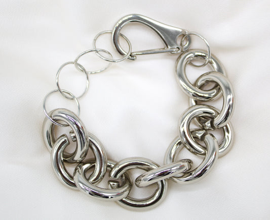 A thick silver chain link bracelet rests on a white satin background, featuring large interlocking links and a secure clasp.