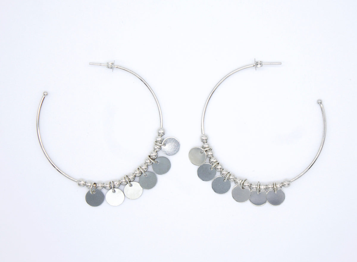 A pair of silver hoop earrings adorned with dangling metallic discs rests against a clean white background.