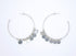 A pair of silver hoop earrings adorned with dangling metallic discs rests against a clean white background.