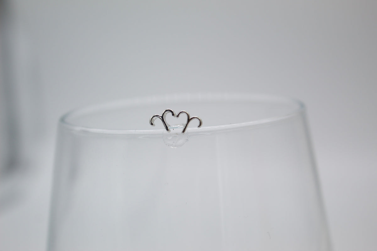 A silver Aries zodiac sign charm rests delicately on the rim of a clear glass.