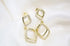 Two dangling gold diamond earrings rest on a soft white satin fabric background.