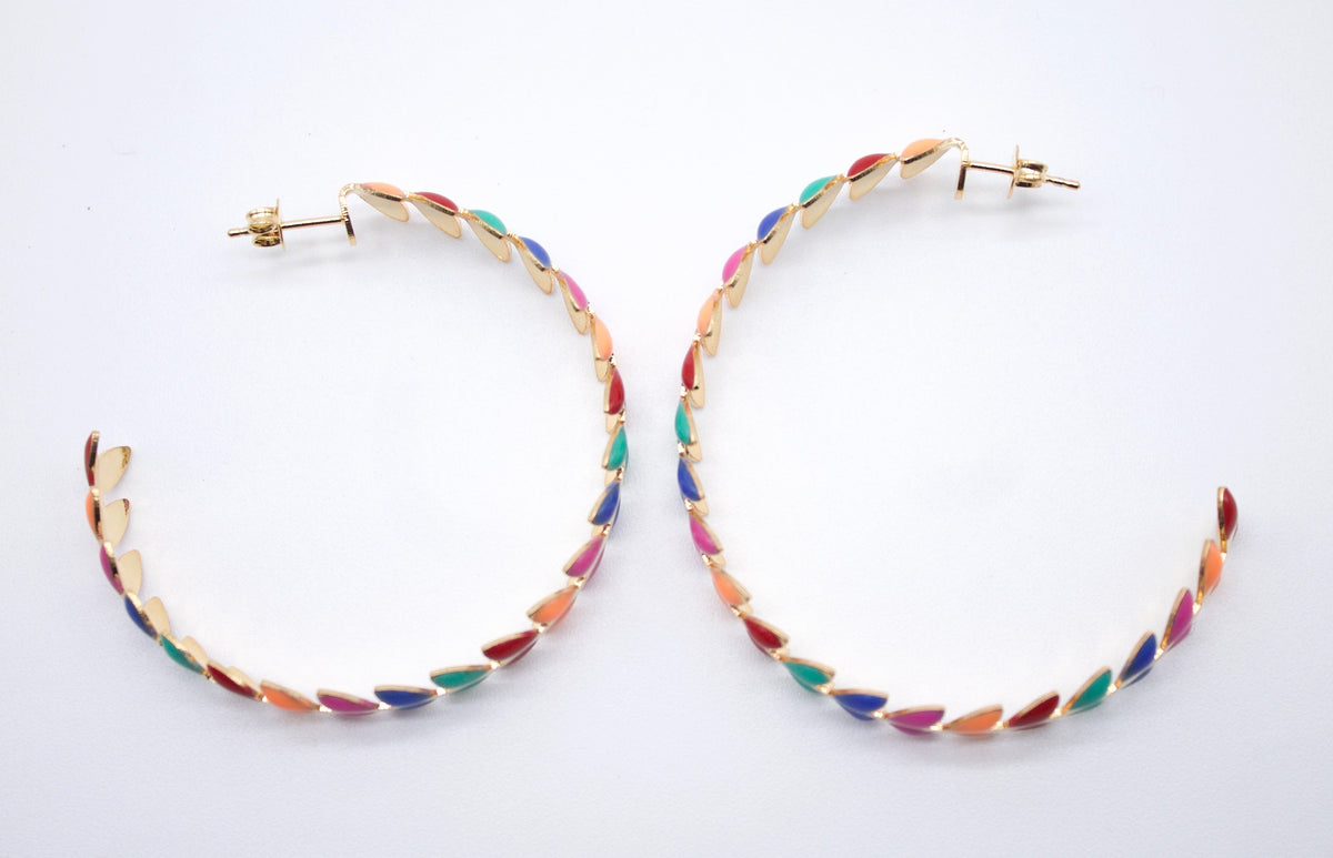 A pair of gold hoop earrings features a vibrant design made of colorful enamel leaves in shades of red, blue, green, pink, and orange.