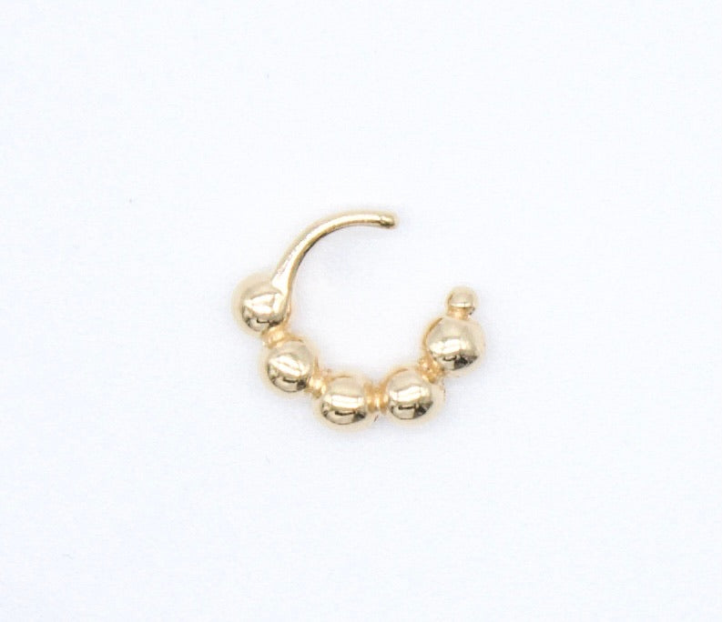 A gold beaded hoop piercing rests against a plain white background.
