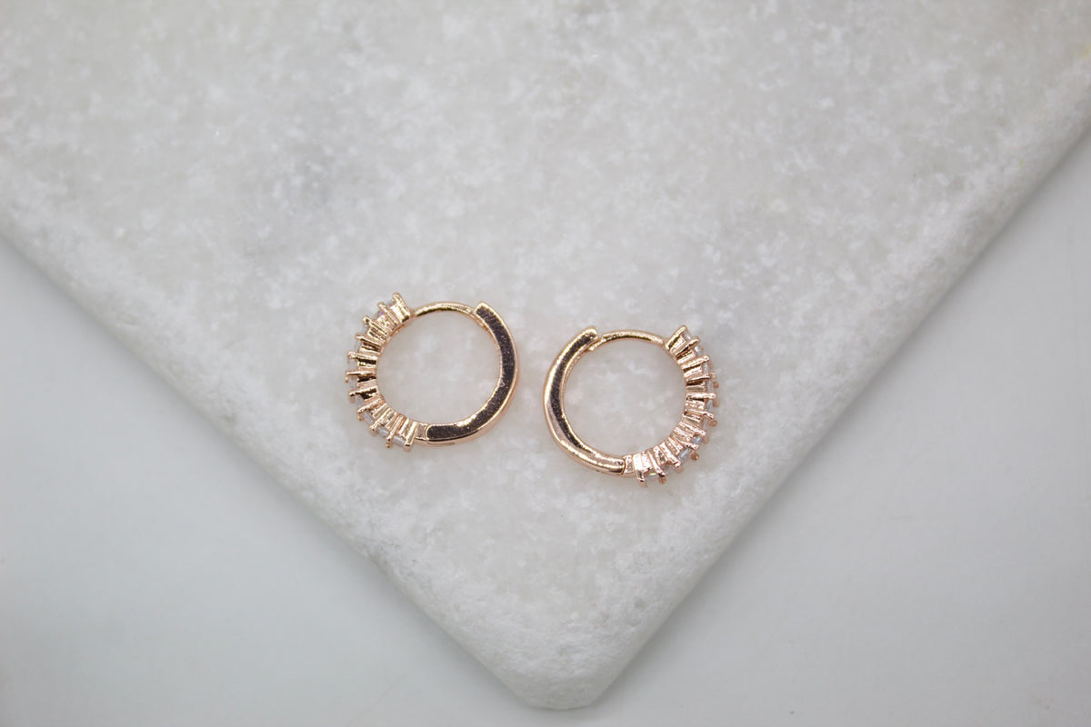 A pair of sparkling rose gold hoop earrings resting on a white marble surface.