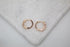 A pair of sparkling rose gold hoop earrings resting on a white marble surface.