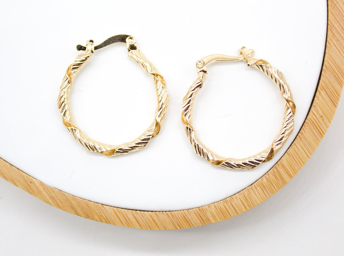 A pair of textured gold huggie hoop earrings rests on a white display surface.
