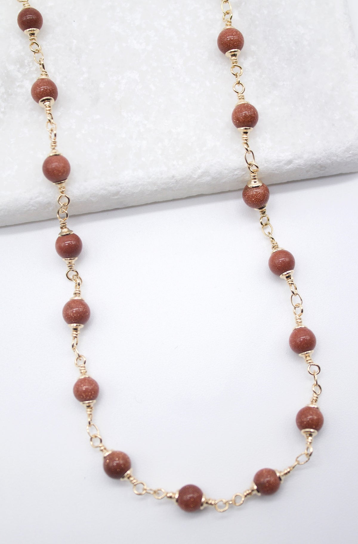 A delicate gold chain necklace features sparkling brown sandstone beads arranged on a white background.