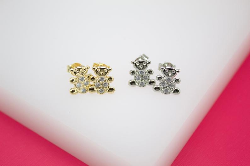 Two pairs of cute gold and silver teddy bear stud earrings feature sparkling cubic zirconia bellies on a white display surface.