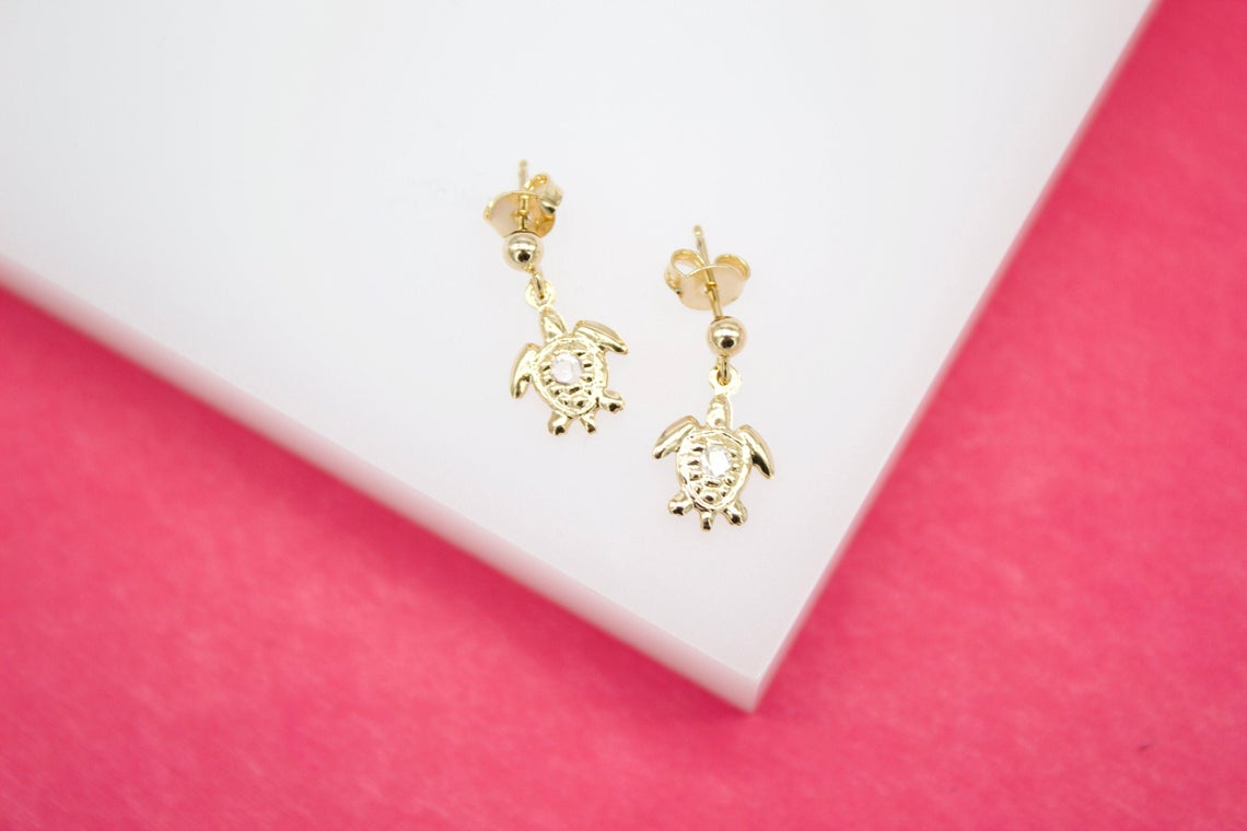 A pair of gold turtle stud earrings featuring sparkling crystal shells rests on a white display surface.