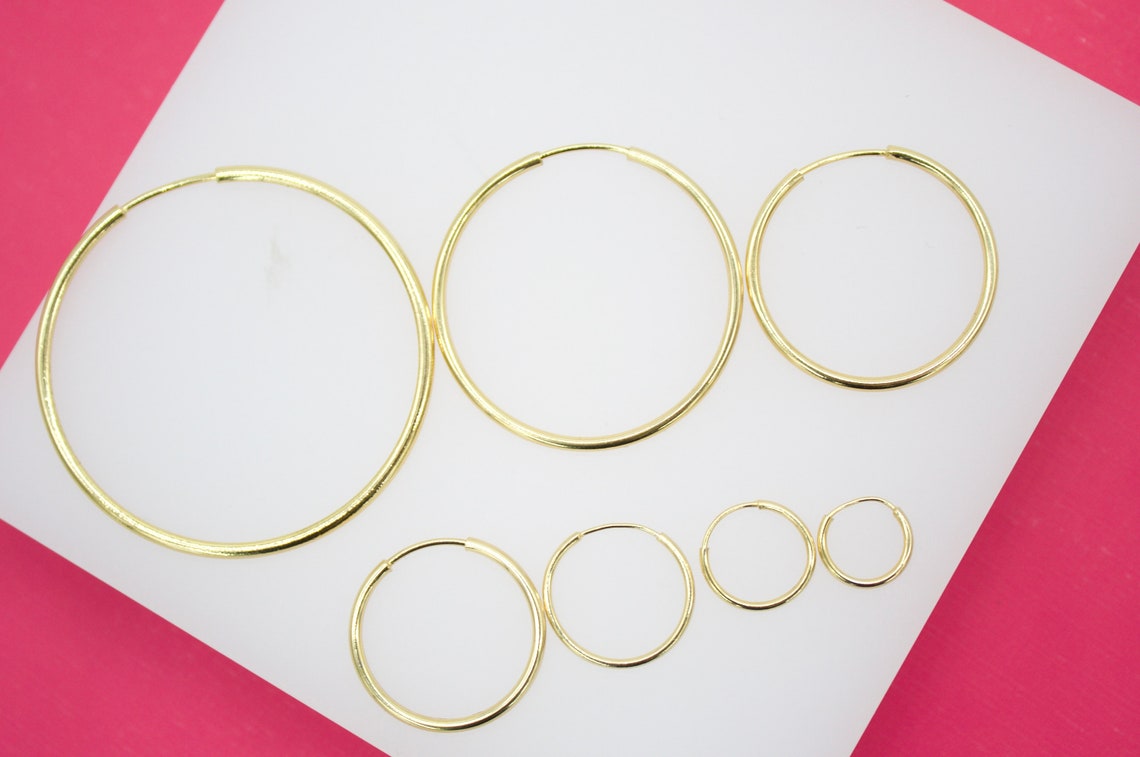 A collection of various sizes of minimalist gold hoop earrings arranged on a white display surface.
