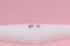 Gold stud earrings spelling "LOVE" with a pave diamond heart resting on a white surface against a pink background.