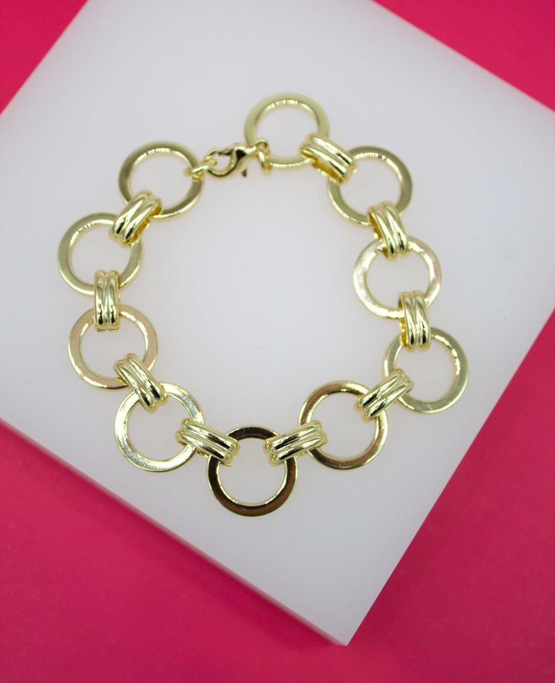 A polished gold link bracelet rests on a white display surface against a vibrant pink background.