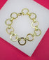 A polished gold link bracelet rests on a white display surface against a vibrant pink background.