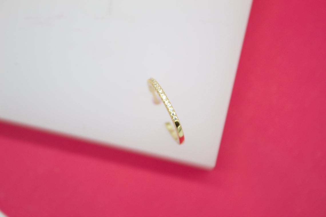 A delicate gold hoop earring encrusted with sparkling cubic zirconia stones rests against a white display block.
