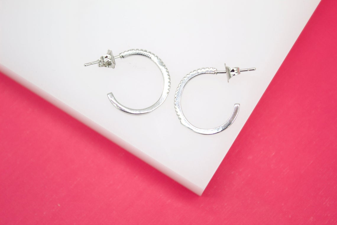 A pair of sparkling silver hoop earrings rests elegantly on a white surface against a vibrant pink background.