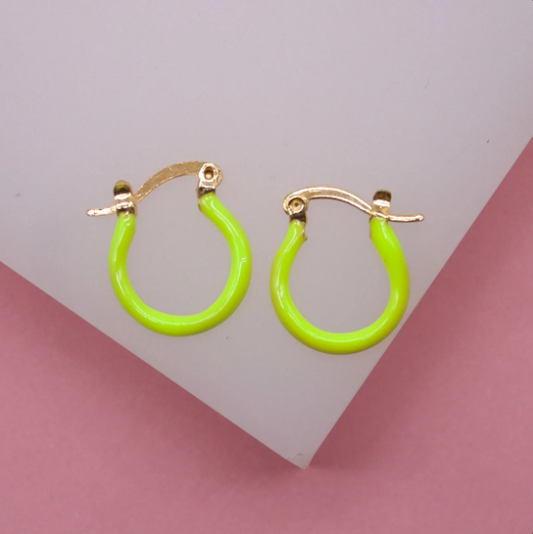 A pair of vibrant neon green and gold hoop earrings rests on a white display surface against a pink background.