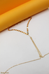 A delicate gold body chain rests on a white and yellow background.